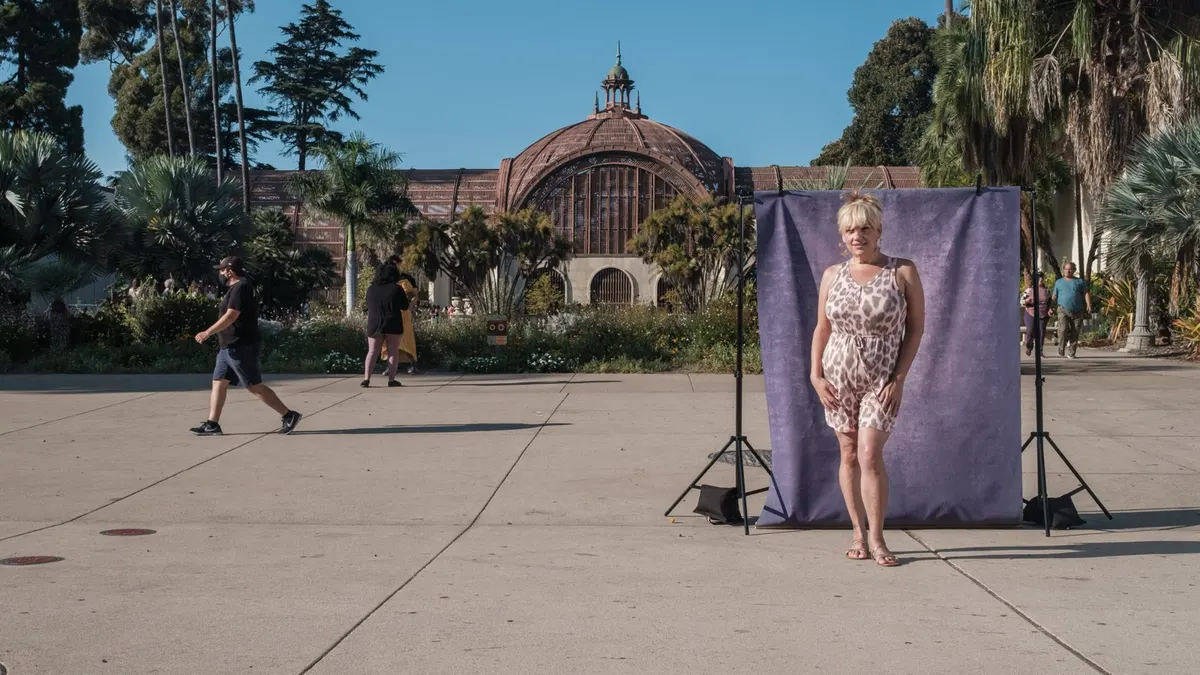 Monique poses in a leopard-print romper in front of a purple backdrop on the Balboa Park promenade, the Botanical Building and gardens behind her.
